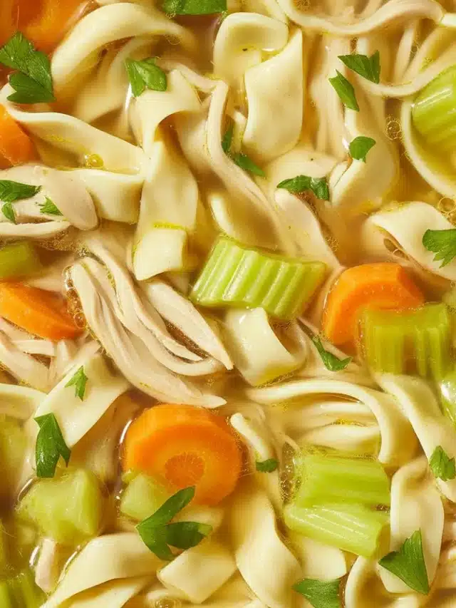 A bowl of steaming homemade chicken noodle soup with vegetables and herbs.