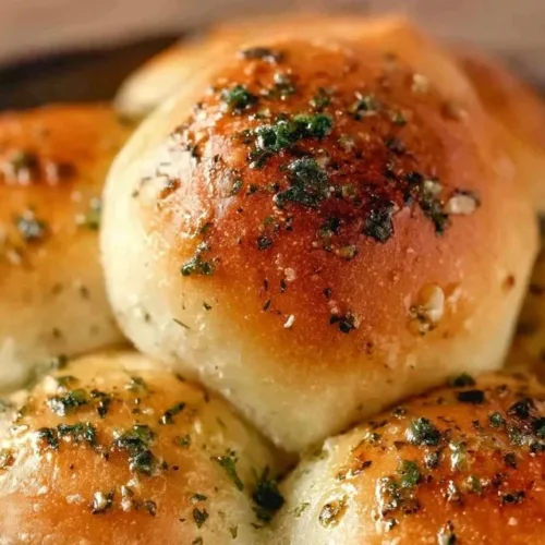 Freshly baked garlic bread rolls served on a wooden platter with herbs.