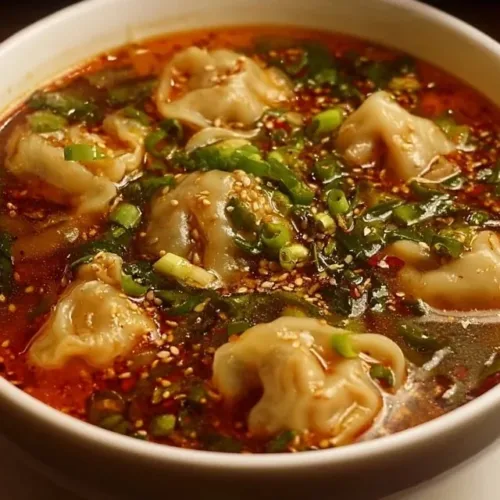 Bowl of spicy dumpling soup with steaming broth and vibrant toppings.